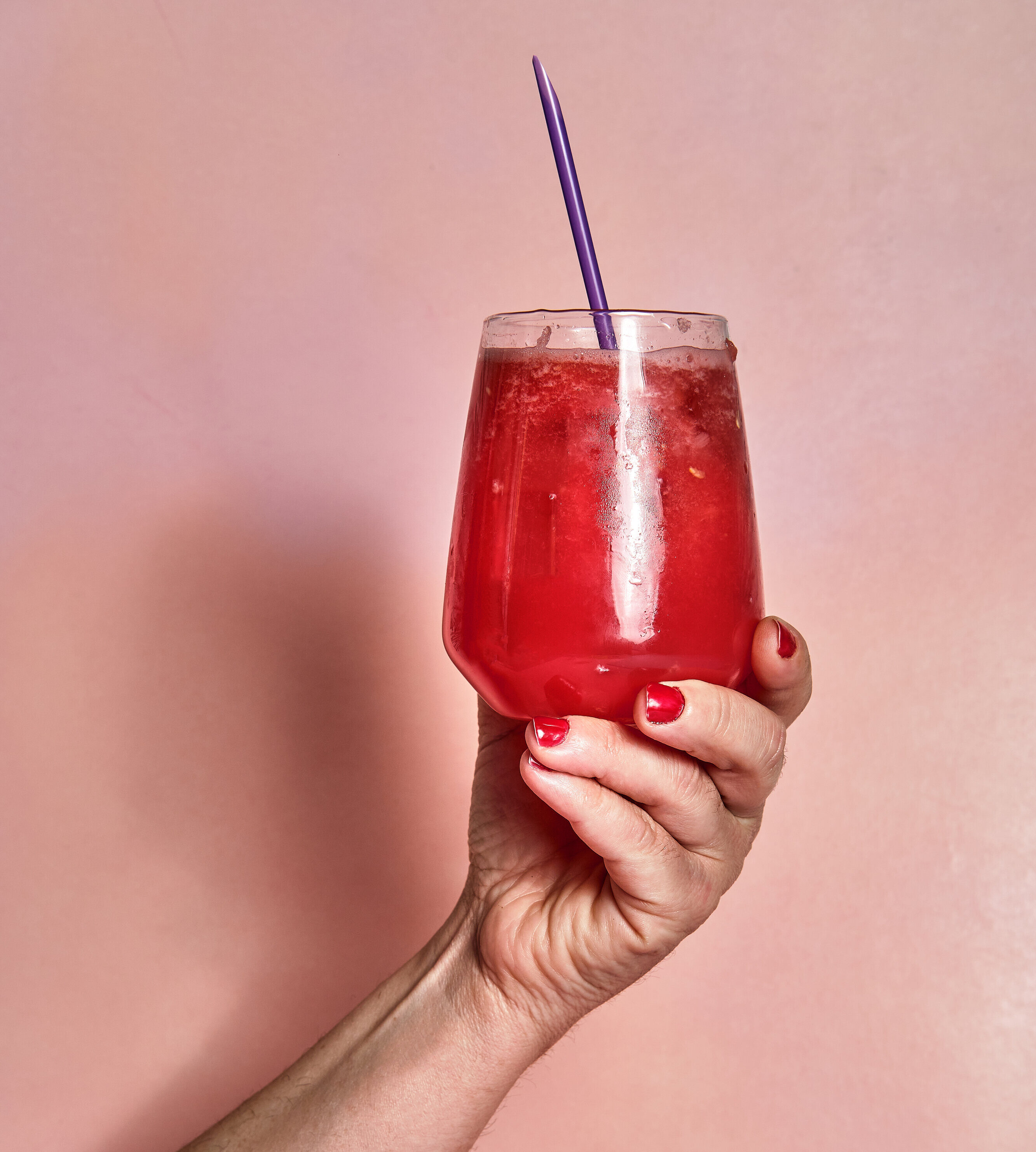 female hand holds glass of summer watermelon soda on pink background and purple straw - Washingtonian