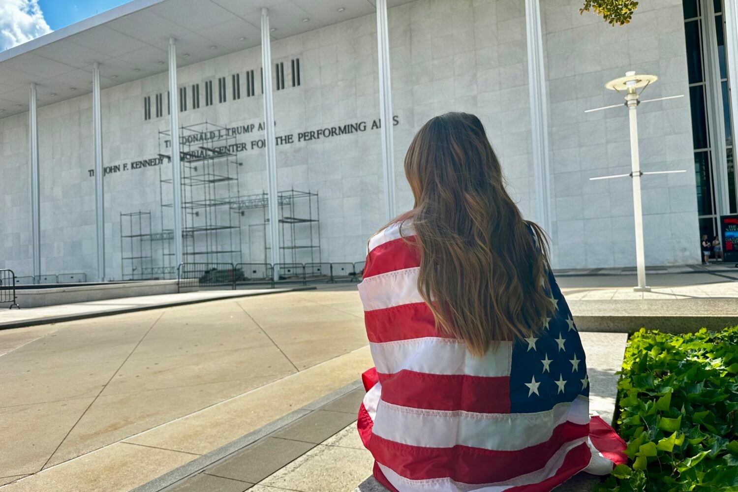 A spectator wrapped in an American flag waits for Donald Trump's name to come off of the Kennedy Center