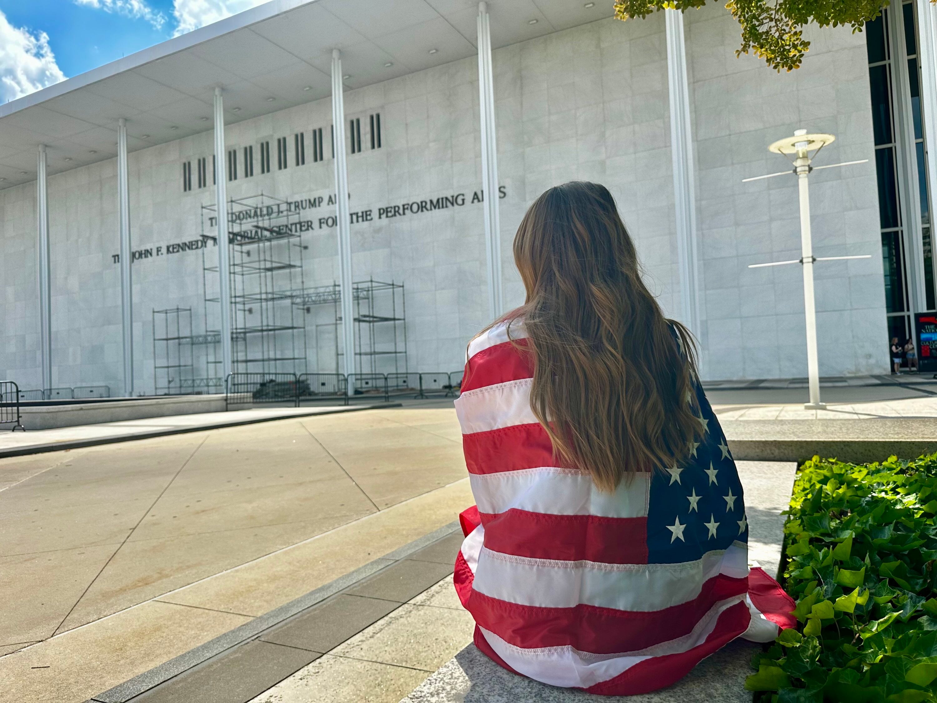 A spectator wrapped in an American flag waits for Donald Trump's name to come off of the Kennedy Center